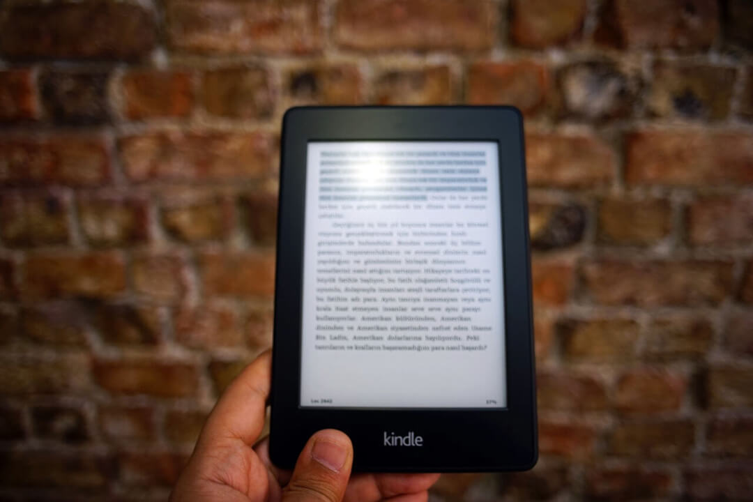  A hand holding a Kindle e-reader in front of a brick wall.